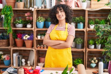 Ortadoğulu genç bir çiçekçi. Çiçekçiye kollarını kavuşturup gülümsüyor.