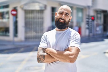 Kel genç adam kollarını kavuşturmuş sokakta el kol hareketi yapıyor.