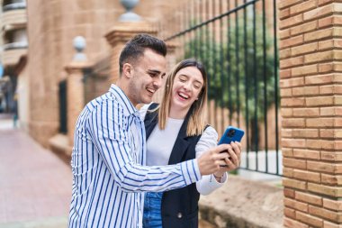 Man and woman couple using smartphone standing together at street