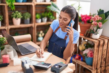 Çiçekçide, çiçekçide, güzel İspanyol bir çiçekçi akıllı telefondan not defterine yazı yazıyor.
