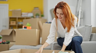 Genç kızıl saçlı kadın yeni evinde karton kutu paketliyor.