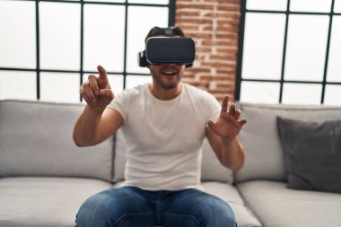 Evde sanal gerçeklik gözlüğü kullanarak video oyunu oynayan İspanyol genç adam.