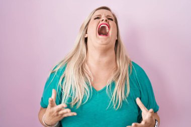 Caucasian plus size woman standing over pink background angry and mad screaming frustrated and furious, shouting with anger. rage and aggressive concept. 