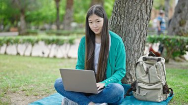 Genç Çinli kadın parkta dizüstü bilgisayar kullanıyor.
