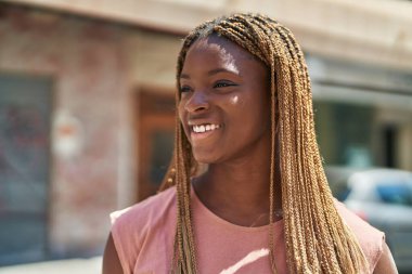 Afro-Amerikalı kadın gülümsüyor. Kendinden emin bir şekilde caddeye bakıyor.