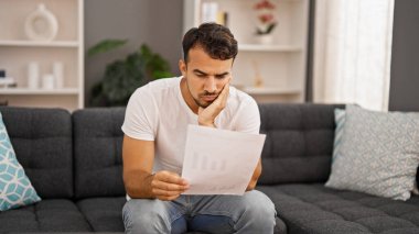 Genç İspanyol adam Bill 'i okuyor. Kanepede oturmuş, üzgün üzgün bakıyor.