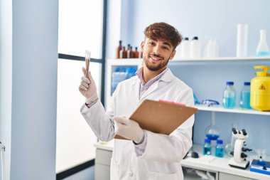 Young arab man scientist holding test tube and clipboard at laboratory