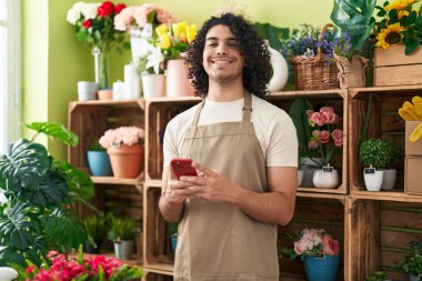 Çiçekçide akıllı telefon kullanarak gülümseyen genç Latin bir çiçekçi.
