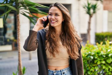 Genç, güzel, İspanyol bir kadın gülümsüyor ve caddede akıllı telefondan konuşuyor.