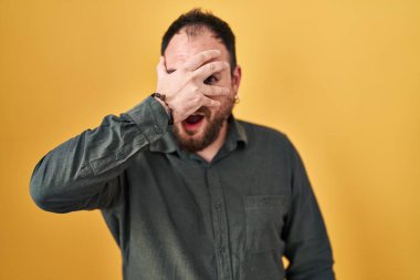 Ayrıca sarı arka planda dikilmiş sakallı İspanyol bir adam. Şok olmuş, yüzünü ve gözlerini kapamış, utangaç ifadesiyle parmaklarının arasından bakıyor.. 