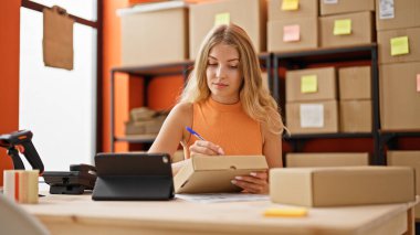 Genç sarışın kadın ecommerce iş işçisi. Ofisteki pakette dokunmatik kağıt kullanıyor.