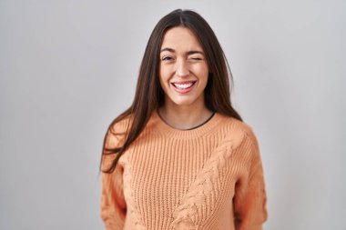 Genç esmer kadın beyaz arka planda duruyor. Seksi bir ifadeyle kameraya bakıyor. Neşeli ve mutlu bir yüzü var.. 