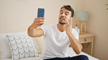 Genç İspanyol adam yatak odasında, akıllı telefonuyla selfie çekiyor.