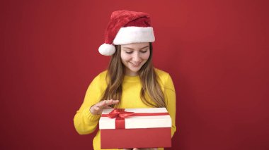 Sarışın, genç bir kadın, Noel şapkası takıyor ve kırmızı arka planda hediyeler tutuyor.