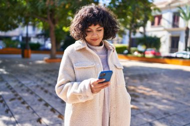 Parkta akıllı telefon kullanarak gülümseyen güzel bir İspanyol kadın.