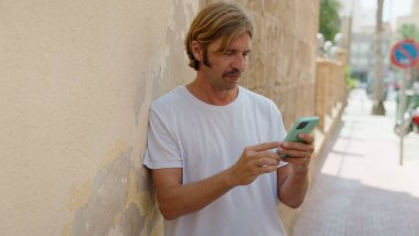 Sokakta akıllı telefon kullanan genç sarışın adam.