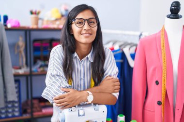 Güzel İspanyol kadın terzi gülümsüyor. Elbise fabrikasında dikiş makinesine yaslanıyor.