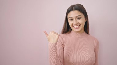 Genç, güzel, İspanyol bir kadın gülümsüyor, pembe arka planda bir kenarı işaret ediyor.