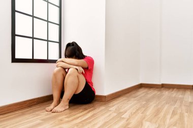 Young beautiful hispanic woman sitting on floor crying at empty room