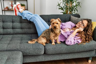 Genç, güzel, İspanyol bir kadın akıllı telefondan konuşuyor. Kanepede köpeğiyle yatıyor.