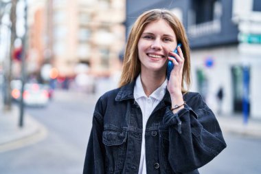 Genç sarışın kadın gülümsüyor. Kendine güveni tam. Akıllı telefondan konuşuyor.