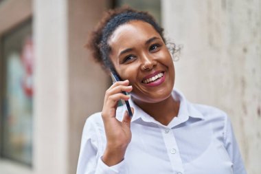 Afro-Amerikalı kadın gülümsüyor. Akıllı telefondan konuşuyor.