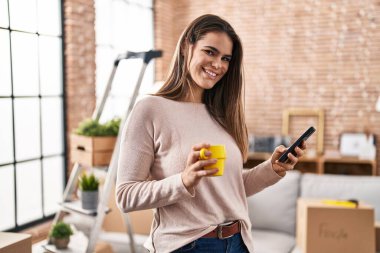 Genç, güzel, İspanyol bir kadın akıllı telefon kullanıyor. Yeni evinde kahve içiyor.