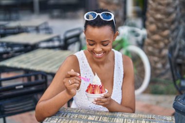 Kahve dükkanının terasında oturmuş dondurma yiyen Afrikalı Amerikalı kadın.