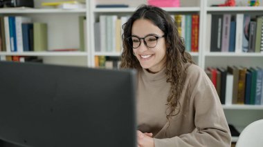 Young beautiful hispanic woman student using computer studying at library university
