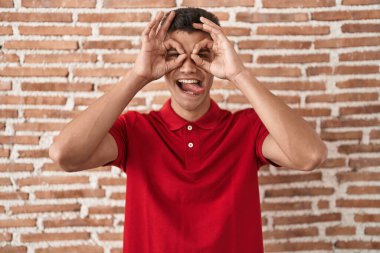 Duvarın başında dikilen genç İspanyol adam dürbün gibi jest yapıyor, gözleri parmaklarından bakıyor. çılgın ifade. 