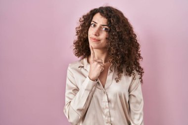 Pembe arka planda duran kıvırcık saçlı İspanyol kadın parmak çenesinde şüpheye yoğunlaşmıştı. 