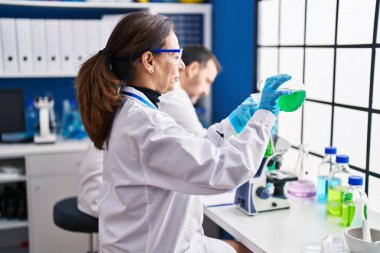 Middle age man and woman scientists measuring liquid at laboratory