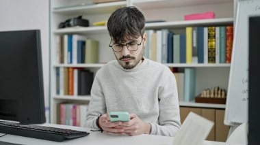 Genç İspanyol öğrenci üniversite sınıfında akıllı telefon kullanıyor.