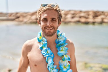 Sahilde beyaz bir adam Hawaii kolyesi takıyor. Olumlu ve mutlu görünüyor. Kendine güvenen bir gülümsemeyle dişlerini gösteriyor. 