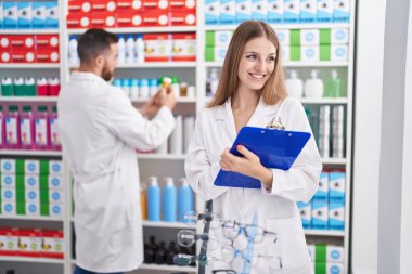 Man and woman pharmacists smiling confident writing on document at pharmacy