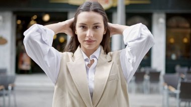 Young beautiful hispanic woman smiling confident combing hair with hands at street