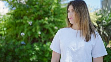 Young blonde woman looking to the side with serious expression at park