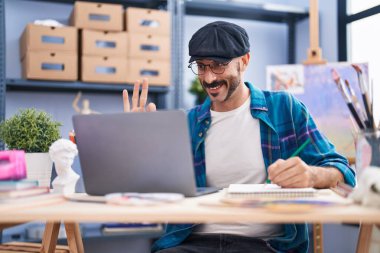 Sakallı İspanyol bir adam sanat stüdyosunda video çekiyor parmaklarıyla imza atıyor, gülümsüyor ve mükemmel bir sembol oluşturuyor. 