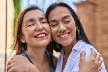 Two women mother and daughter smiling confident hugging each other at street