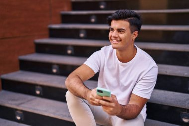 Genç İspanyol adam akıllı telefon kullanıyor. Merdivenlerde oturuyor.