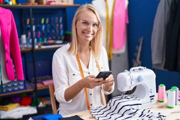 Young Blonde Woman Tailor Smiling Confident Using Smartphone Sewing Studio — Zdjęcie stockowe