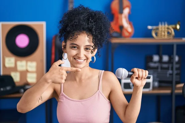 stock image Hispanic woman with curly hair singing song using microphone at music studio smiling happy pointing with hand and finger 