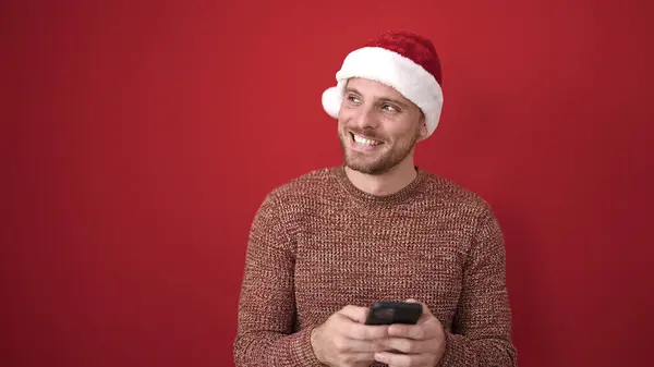 Junger Kaukasischer Mann Lächelt Mit Smartphone Und Trägt Weihnachtsmütze Vor — Stockfoto