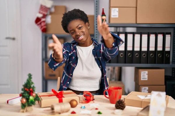 stock image African american woman working at small business doing christmas decoration looking at the camera smiling with open arms for hug. cheerful expression embracing happiness. 