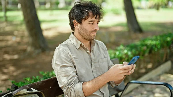 Молодой Латиноамериканец Использует Смартфон Серьезным Выражением Лица Сидя Скамейке Парке — стоковое фото