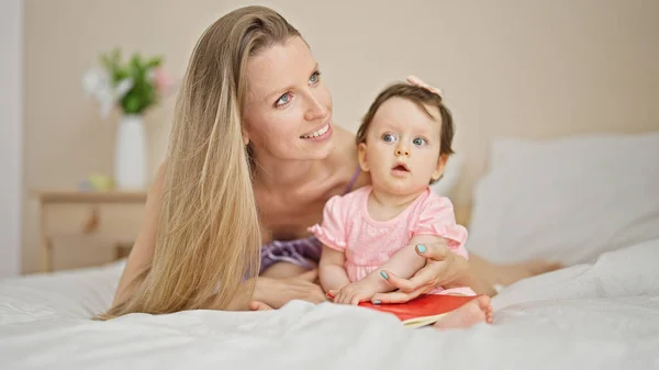 Mother and daughter lying on bed holding book at bedroom