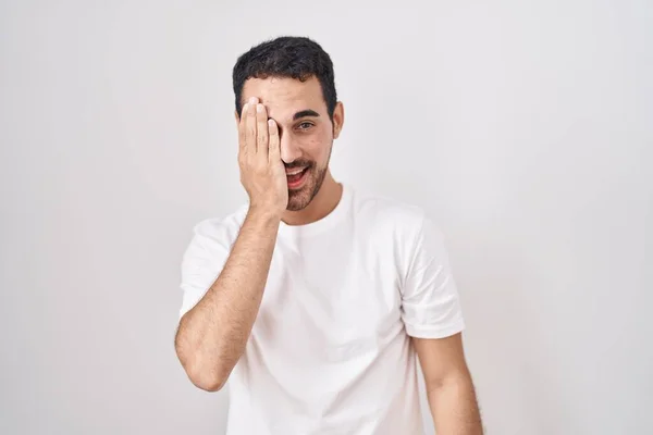 Pohledný Hispánec Stojící Nad Bílým Pozadím Zakrývající Jedno Oko Rukou — Stock fotografie