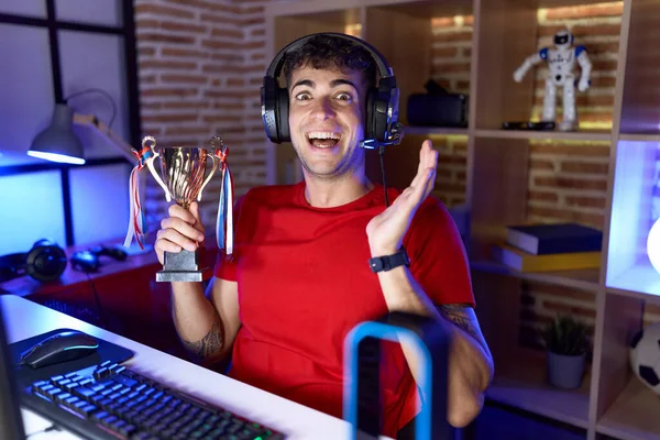 Νεαρός Ισπανός Που Παίζει Βιντεοπαιχνίδια Κρατώντας Τρόπαιο Γιορτάζοντας Επίτευγμα Χαρούμενο — Φωτογραφία Αρχείου