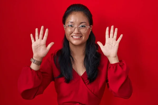 stock image Asian young woman standing over red background showing and pointing up with fingers number ten while smiling confident and happy. 