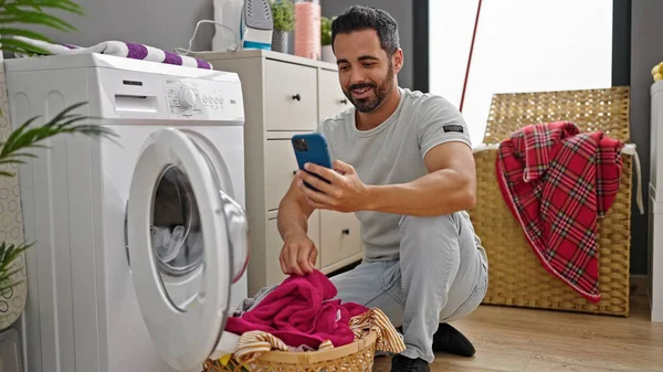 Ung Latinamerikan Man Med Smartphone Tvätta Kläder Ler Mot Tvättstuga — Stockfoto